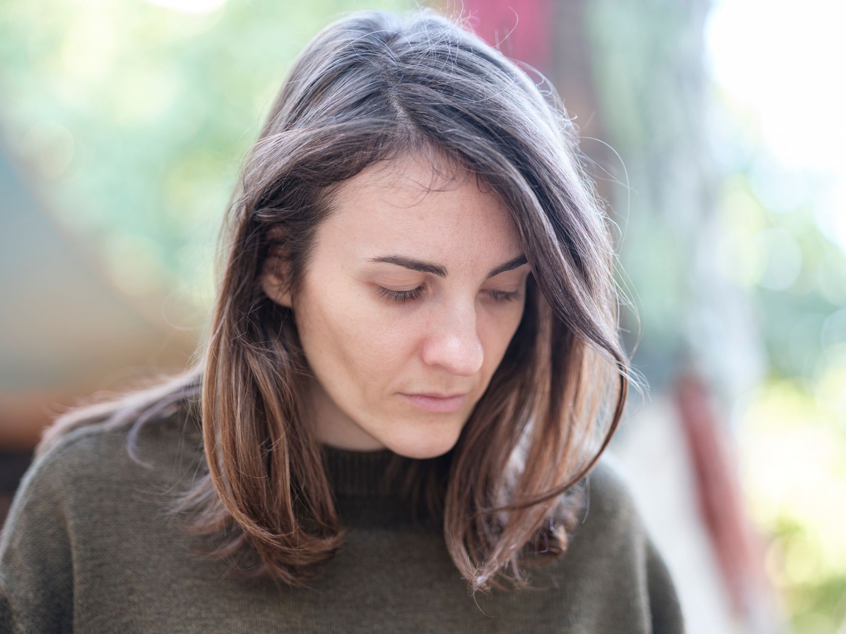 Young woman with thoughtful expression outdoors, bathed in gentle sunlight, evoking introspection.