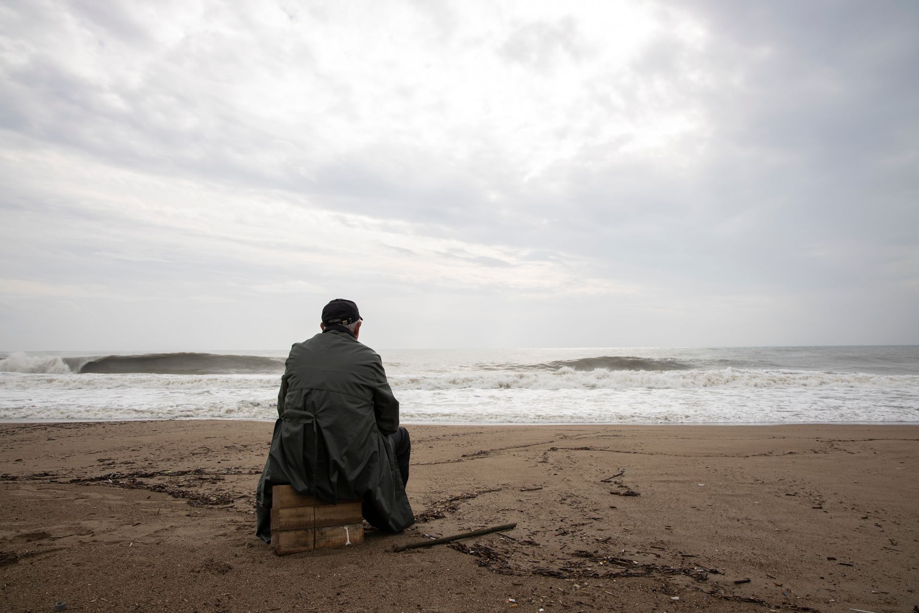 A man sitting alone on an empty beach looking at the stormy sea, evoking thoughts of solitude and reflection.