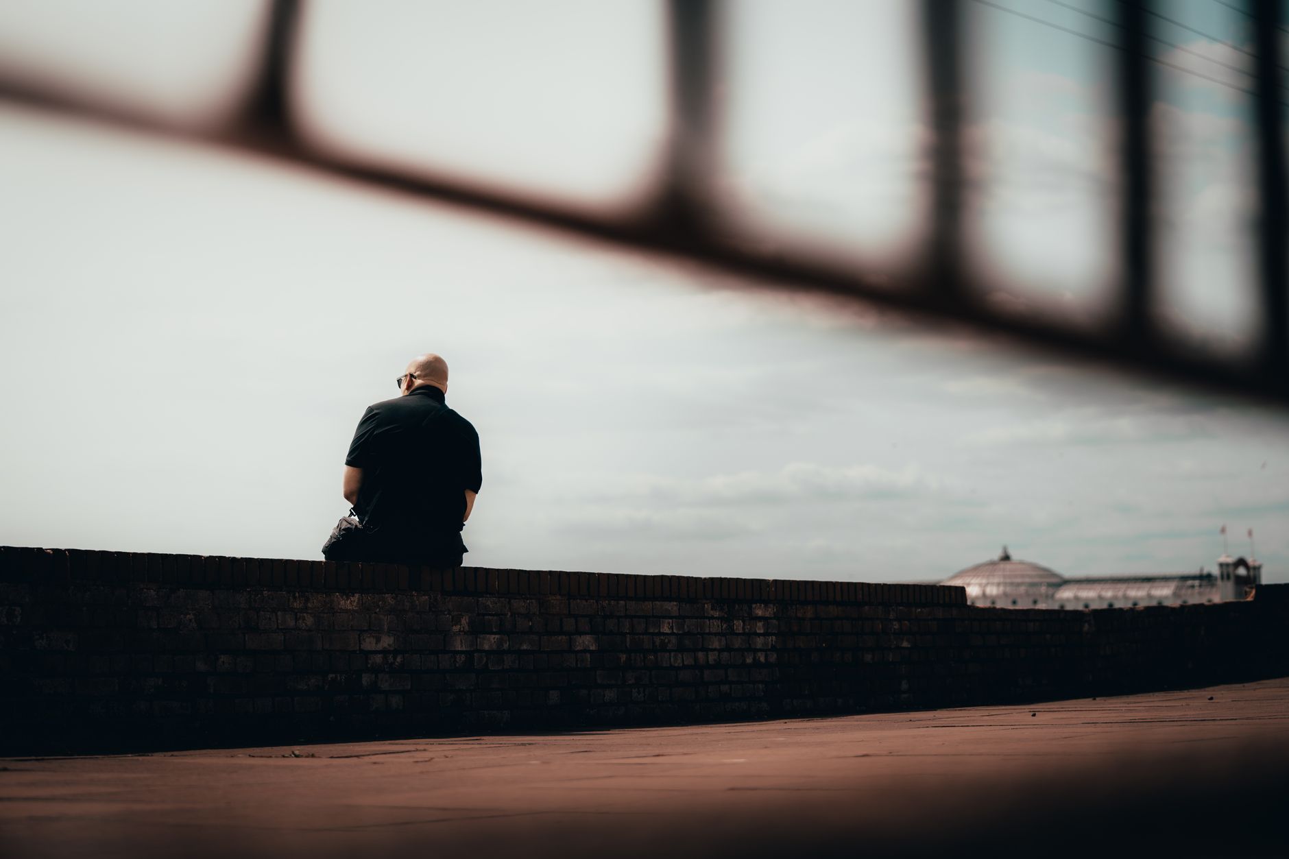 A solitary man sits contemplatively on a wall in Brighton and Hove, England.