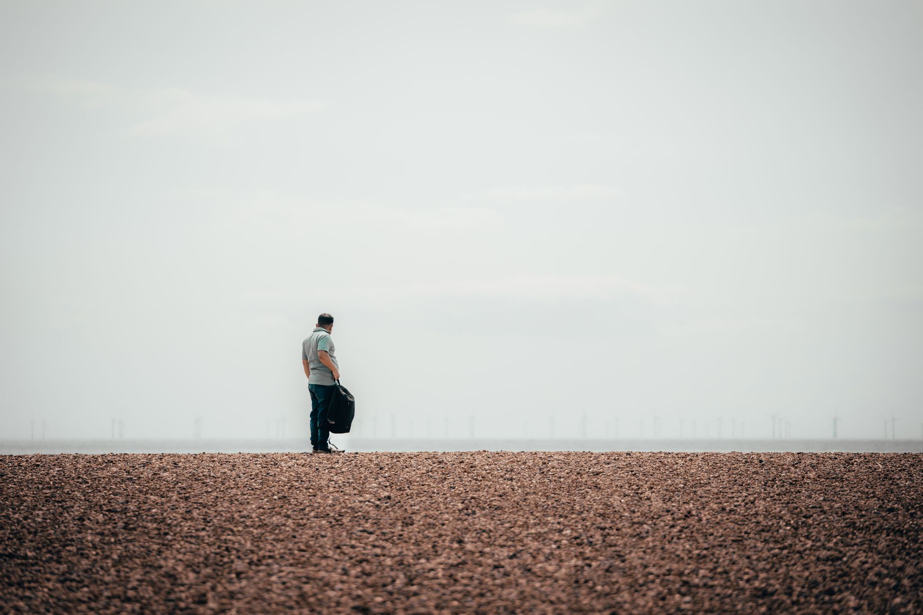 A person stands alone on the vast pebbled beach of Brighton, capturing a serene and contemplative moment.