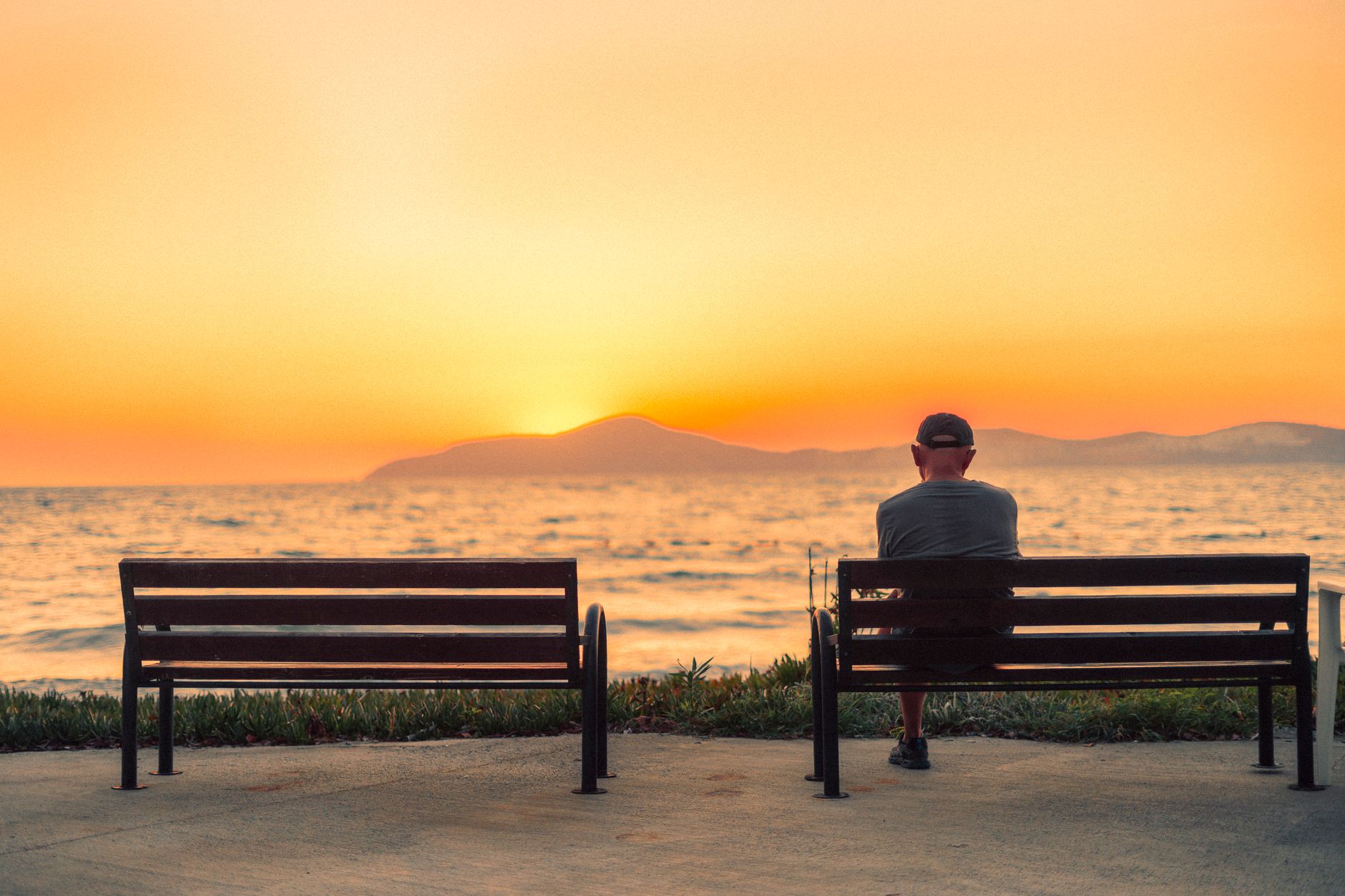 Silhouette of a man on a bench watching a peaceful sunset over the Aegean Sea in Güllük, Turkey.
