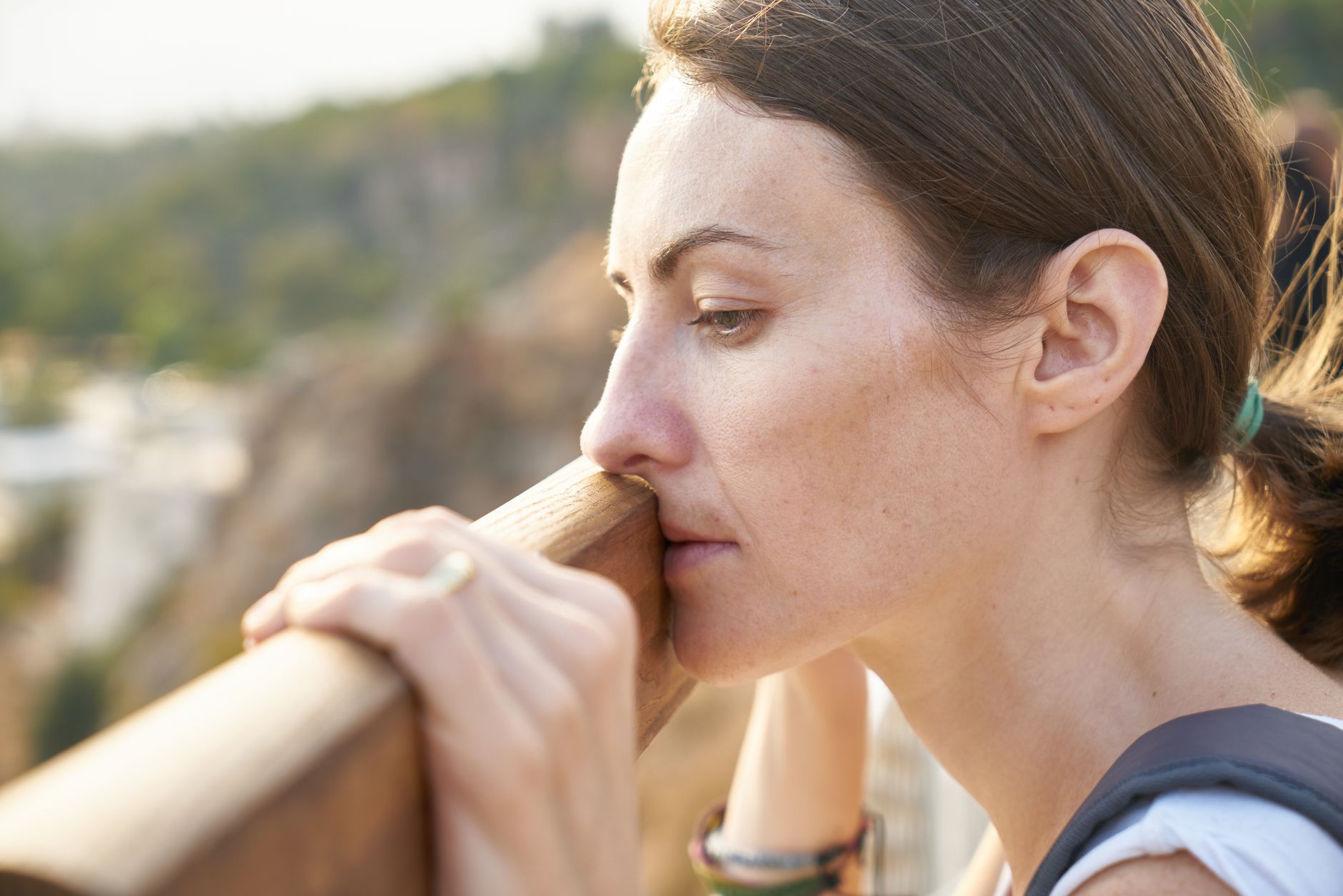 A thoughtful woman leans on a railing, lost in deep contemplation outdoors.