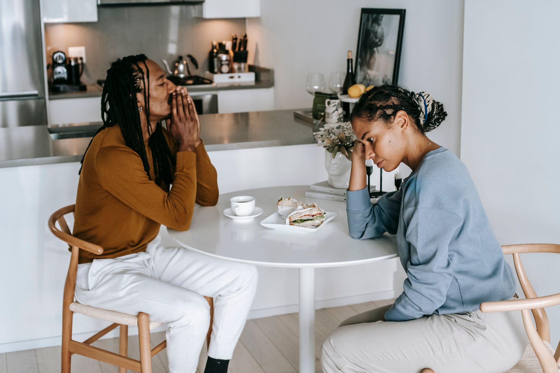 Young African American man sitting at table with woman and looking down thoughtfully while having conflict