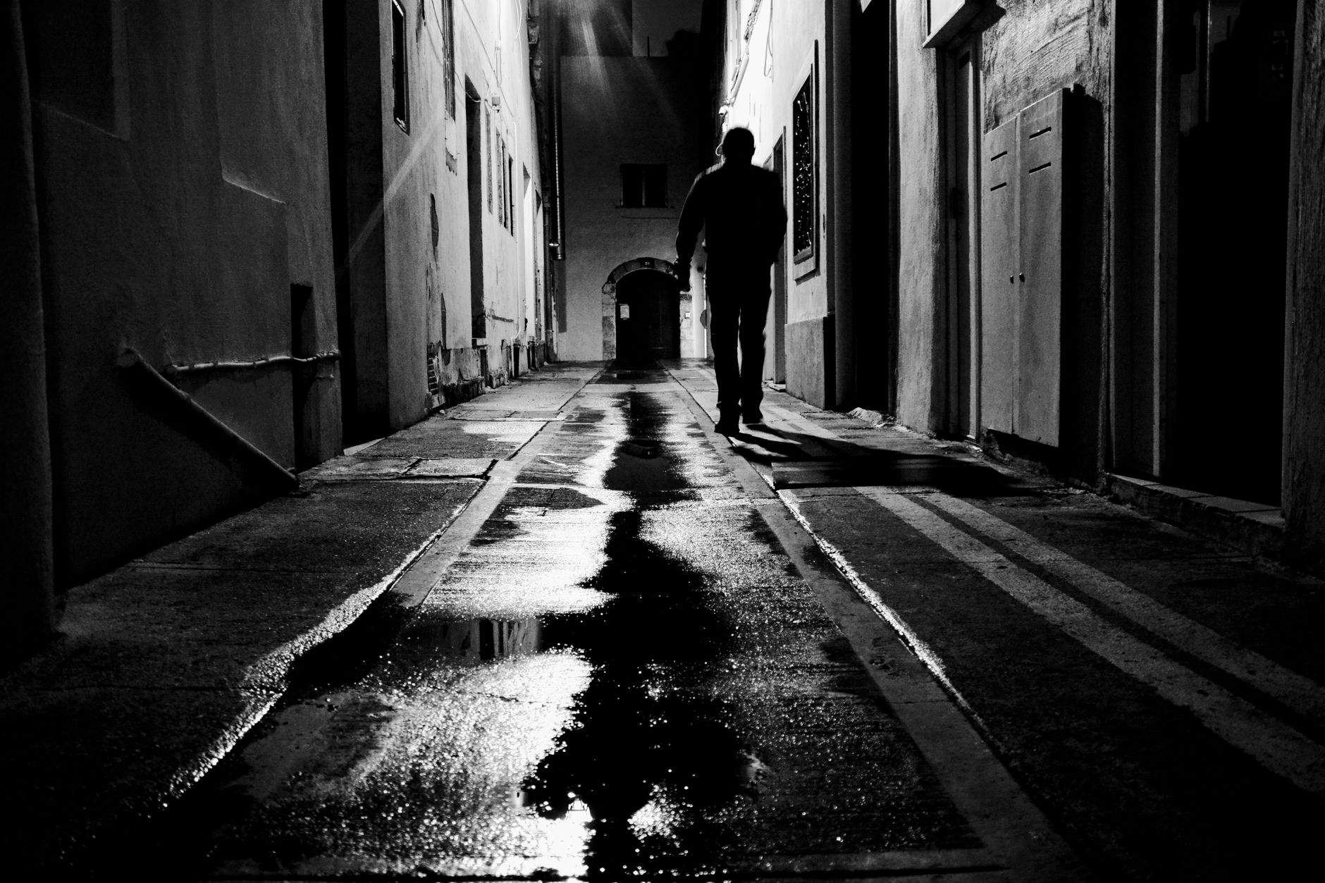A lone figure walks through a dimly lit alley in Naxxar, Malta, on a rainy night.