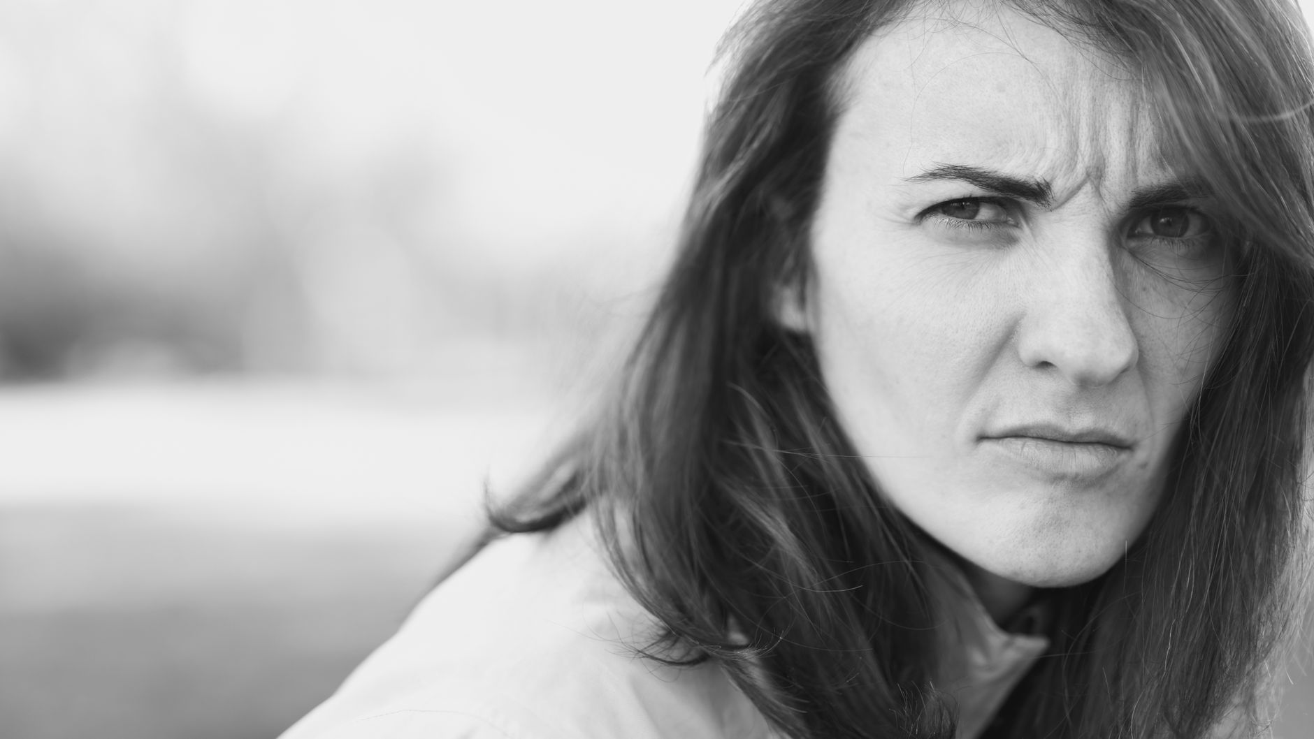 Close-up monochrome portrait of a young woman looking pensive outdoors.
